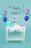 mermaid and narwhal themed party setting with a birthday banner, mermaid garland, cupcake toppers, balloons and gift bags